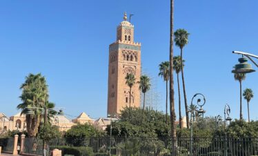 12 Days Morocco Desert Tour ,A long caravan of camels walks along the crest of the golden sand dunes of the Sahara Desert under a setting sun, during a 12-day tour from Marrakech.,A small group of travelers, wearing turbans and smiling, ride camels on a tour through the Erg Chebbi dunes on a 12-day desert expedition from Marrakech.,The ancient earthen kasbah of Ait Benhaddou, a UNESCO World Heritage site, bathed in morning light, a key stop on a 12-day Morocco tour from Marrakech to the desert.,A tourist and a local Berber guide share a pot of mint tea inside a traditional desert camp tent during a 12-day Morocco desert tour.