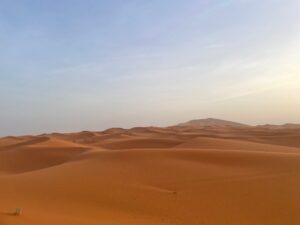 4 Days Marrakech To erg Chiegaga,,Aerial view of the vast golden sand dunes of Erg Chegaga on a 4-day desert tour from Marrakech..Scenic drive through the Tizi n'Tichka pass in the High Atlas Mountains on the way to Erg Chegaga from Marrakech.Lush green palm groves and ancient kasbahs along the Draa Valley during a Morocco desert tour.4x4 desert adventure on the off-road plains leading to the remote Erg Chegaga dunes..Small group on a sunset camel trek across the Erg Chegaga sand dunes during a 4-day Morocco tour..Tourist enjoying sandboarding down the steep slope of a dune in Erg Chegaga desert.,Berber desert camp experience with travelers around a campfire under the stars at Erg Chegaga..A friendly Berber guide serving traditional Moroccan mint tea at a desert camp in Erg Chegaga..Travelers sharing a traditional Moroccan tagine dinner inside a Berber tent at Erg Chegaga..Berber musicians performing traditional music for guests at an Erg Chegaga luxury desert camp..Luxury Berber camp with traditional tents nestled at the foot of the Erg Chegaga dunes.,Cozy and comfortable interior of a desert tent at a camp in Erg Chegaga after a day of exploration..Evening atmosphere at a desert camp in Erg Chegaga, with lanterns lighting up the tents against the dark sky.
