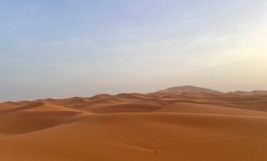 4 Days Marrakech To erg Chiegaga,,Aerial view of the vast golden sand dunes of Erg Chegaga on a 4-day desert tour from Marrakech..Scenic drive through the Tizi n'Tichka pass in the High Atlas Mountains on the way to Erg Chegaga from Marrakech.Lush green palm groves and ancient kasbahs along the Draa Valley during a Morocco desert tour.4x4 desert adventure on the off-road plains leading to the remote Erg Chegaga dunes..Small group on a sunset camel trek across the Erg Chegaga sand dunes during a 4-day Morocco tour..Tourist enjoying sandboarding down the steep slope of a dune in Erg Chegaga desert.,Berber desert camp experience with travelers around a campfire under the stars at Erg Chegaga..A friendly Berber guide serving traditional Moroccan mint tea at a desert camp in Erg Chegaga..Travelers sharing a traditional Moroccan tagine dinner inside a Berber tent at Erg Chegaga..Berber musicians performing traditional music for guests at an Erg Chegaga luxury desert camp..Luxury Berber camp with traditional tents nestled at the foot of the Erg Chegaga dunes.,Cozy and comfortable interior of a desert tent at a camp in Erg Chegaga after a day of exploration..Evening atmosphere at a desert camp in Erg Chegaga, with lanterns lighting up the tents against the dark sky.