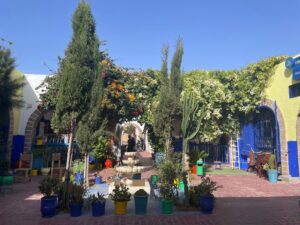 9 days morocco desert tour,A collage representing a 9-day Morocco tour: a camel train at sunset on golden Sahara dunes, the ancient clay buildings of Ait Ben Haddou, the blue-painted streets of Chefchaouen, and a vibrant Marrakech souk.A line of camels walking along the crest of the golden Erg Chebbi dunes at sunset, with their shadows stretching long. A traditional Berber desert camp with cozy tents at the foot of large, smooth sand dunes under a starry night sky.,A winding road cutting through the dramatic, reddish-brown peaks of the High Atlas Mountains. The tall, narrow canyon walls of Todra Gorge with a small river flowing at the bottom.,The ancient earthen Ksar of Ait Ben Haddou, a fortified village with tall clay buildings, set against a desert backdrop. The intricate green-tiled roof and minaret of a royal building in the imperial city of Fes.,The famous blue-washed walls and doorways of the medina in Chefchaouen, the Blue City. A bustling, colorful souk in Marrakech with stalls selling spices, lanterns, and traditional crafts. The wide, elegant streets and modern Hassan Tower in the capital city of Rabat.